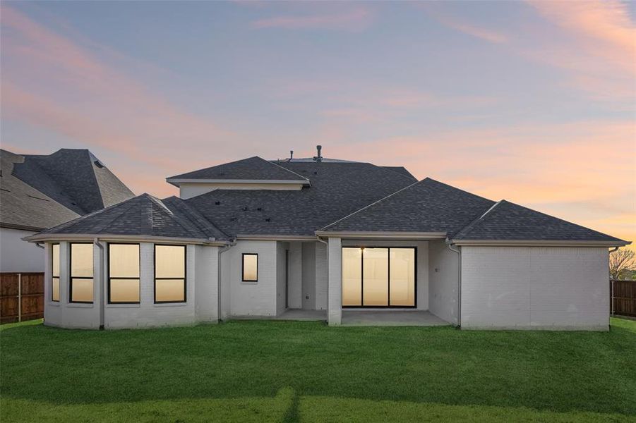 Back of property at dusk featuring a shingled roof, a patio area, and brick siding Back of property at dusk featuring a shingled roof, a patio area, and brick siding