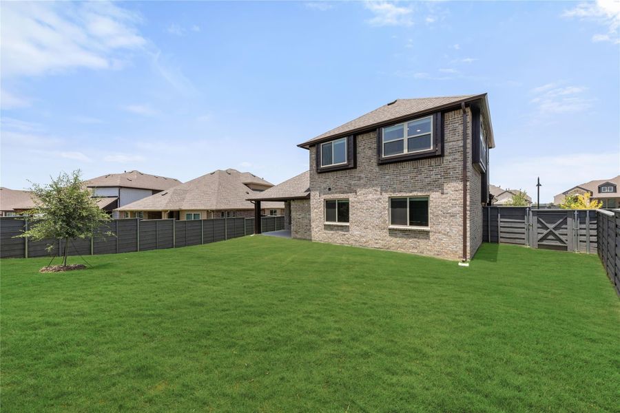 Two-story brick home with large fenced backyard and green lawn viewed from rear exterior Two-story brick home with large fenced backyard and green lawn viewed from rear exterior