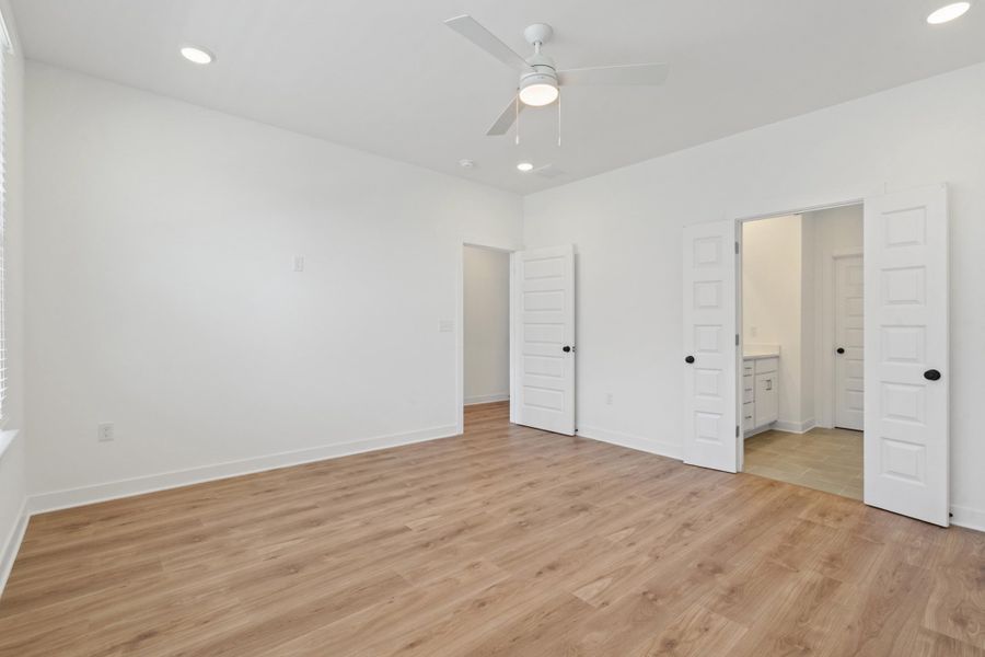 Spacious room featuring wood-finish flooring, white walls, and a ceiling fan