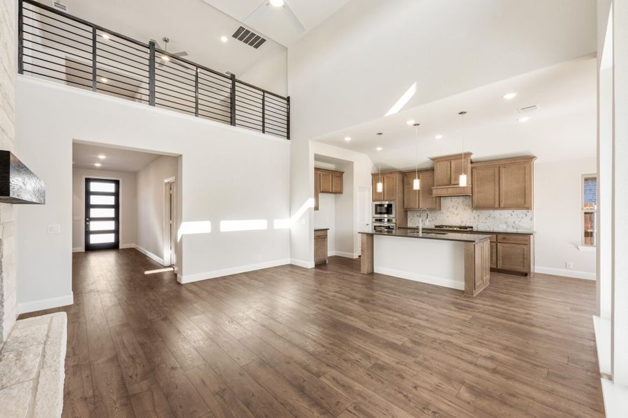 Open-concept living area with two-story ceiling, hardwood floors, and kitchen with island and wood cabinets Open-concept living area with two-story ceiling, hardwood floors, and kitchen with island and wood cabinets