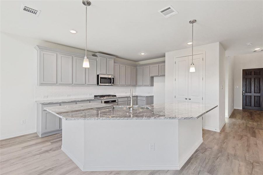 Kitchen featuring a large island, light hardwood / wood-style floors, appliances with stainless steel finishes, and sink