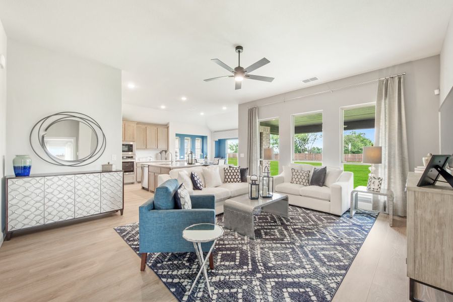 Open-concept living room with ceiling fan, light wood floors, and kitchen visible in background
