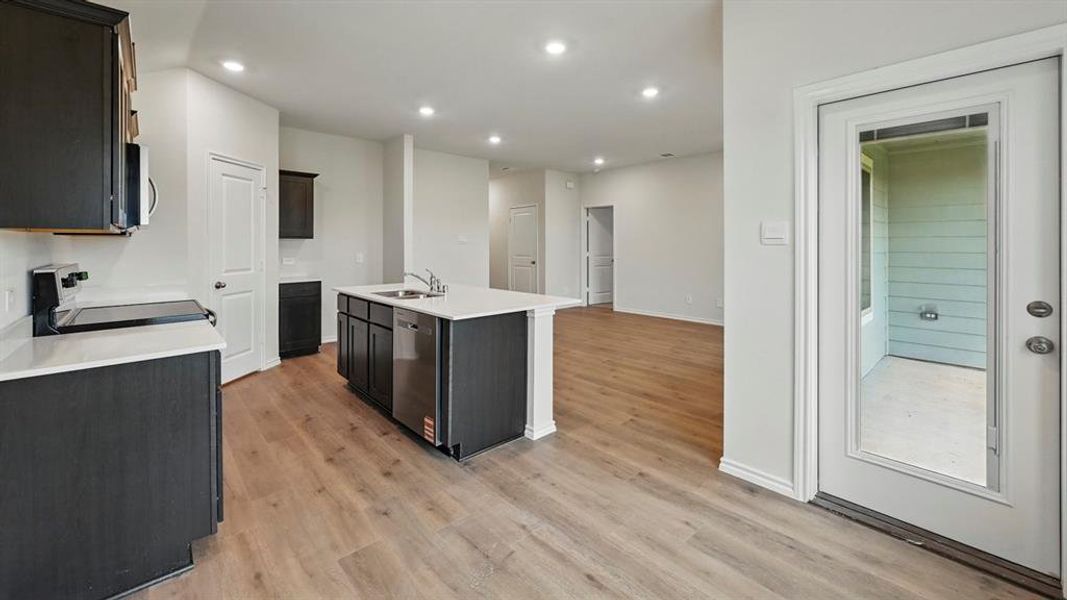 Kitchen featuring recessed lighting, appliances with stainless steel finishes, a center island with sink, light wood-style floors, and light stone countertops