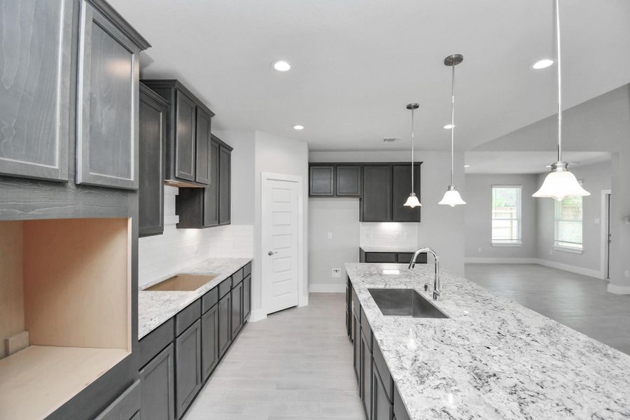The kitchen is a culinary haven, featuring granite countertops, a tile backsplash, stainless steel appliances, 42” upper cabinets, and undercabinet lighting. Sample photo of completed home with similar floor plan. Actual colors and selections may vary.