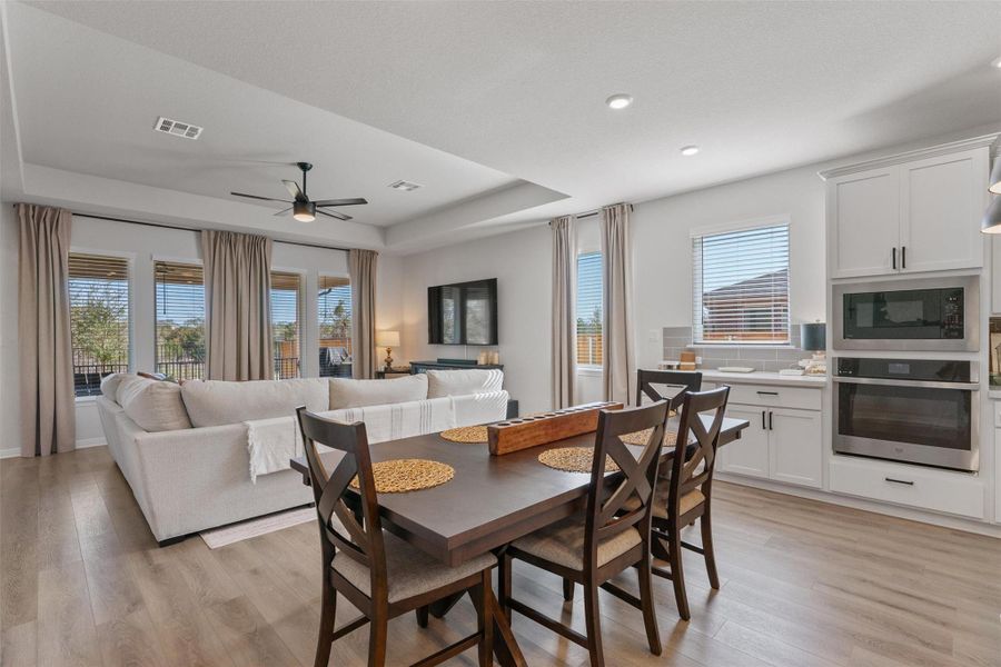 Dining area featuring ceiling fan, light wood finished floors, a tray ceiling, and recessed lighting