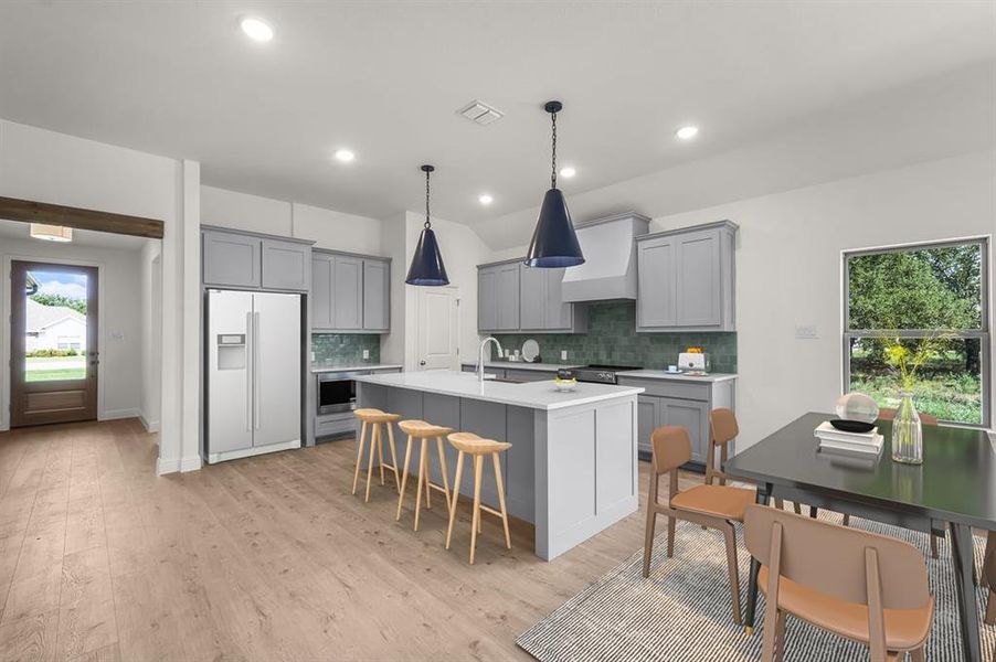 Virtually staged kitchen featuring gray cabinets, white fridge with ice dispenser, a breakfast bar, an island with sink, and light finished floors