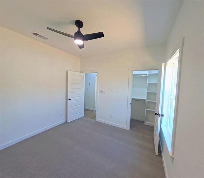 Unfurnished bedroom with a walk in closet, carpet flooring, and ceiling fan Unfurnished bedroom with a walk in closet, carpet flooring, and ceiling fan