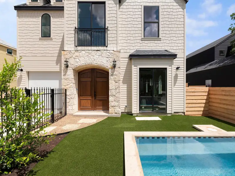 A striking facade with a rustic stone archway welcomes guests to this inviting residence, featuring a private pool and manicured lawn.