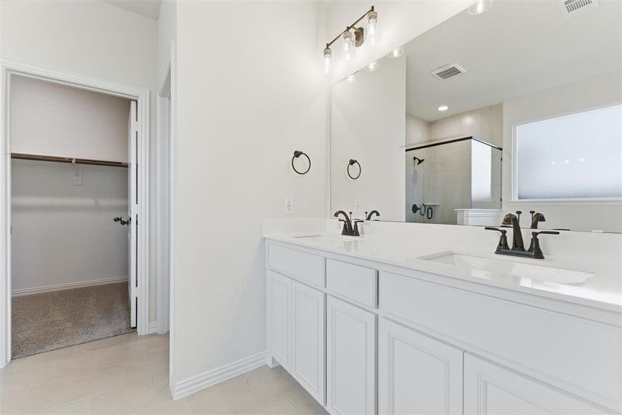 Full bath featuring a spacious closet, a stall shower, double vanity, and light tile patterned flooring