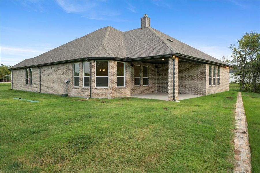 Rear view of property featuring roof with shingles, brick siding, a lawn, a patio area, and a chimney