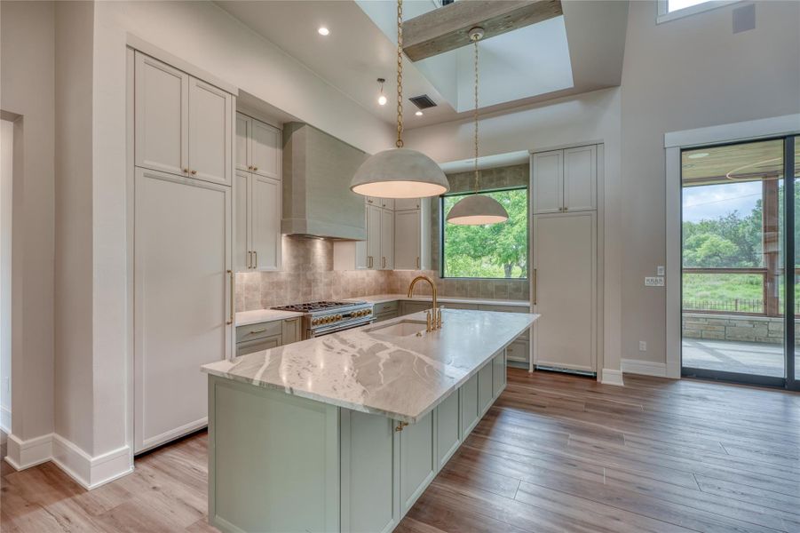 Kitchen featuring wall chimney exhaust hood, a sink, double oven range, baseboards, and plenty of natural light