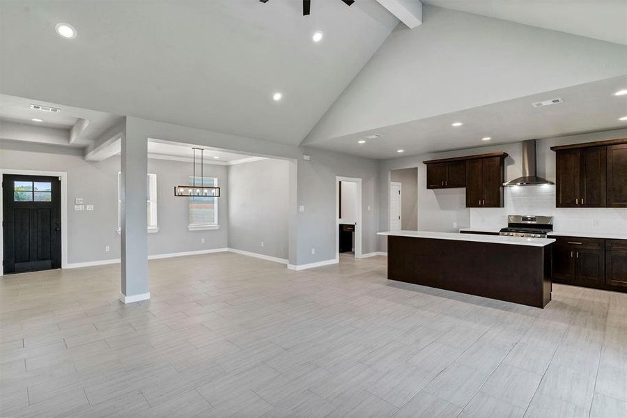 Kitchen with wall chimney exhaust hood, high vaulted ceiling, a center island, light hardwood / wood-style floors, and stainless steel range with gas cooktop