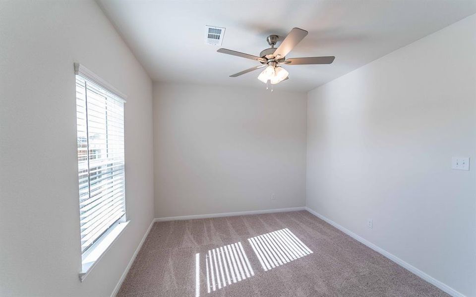 Bright interior space featuring a window with horizontal blinds, neutral-toned carpeting, and a ceiling fan with integrated lighting