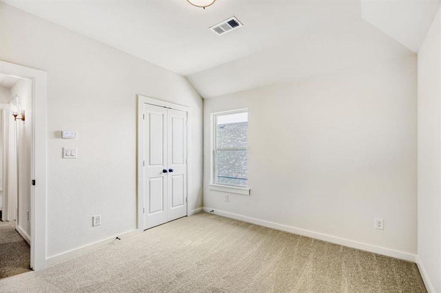 Carpeted room featuring white walls, a vaulted ceiling, a double-door closet, and a window with white trim
