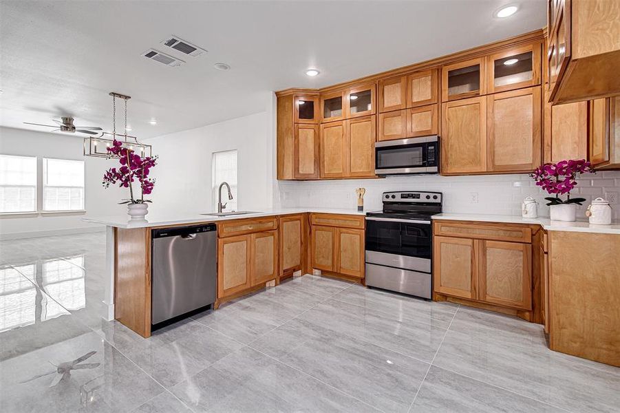 Kitchen with appliances with stainless steel finishes, tasteful backsplash, decorative light fixtures, recessed lighting, and glass insert cabinets