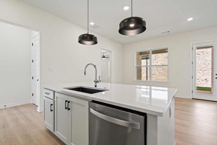 Kitchen with stainless steel dishwasher, light wood-style flooring, an island with sink, and hanging light fixtures
