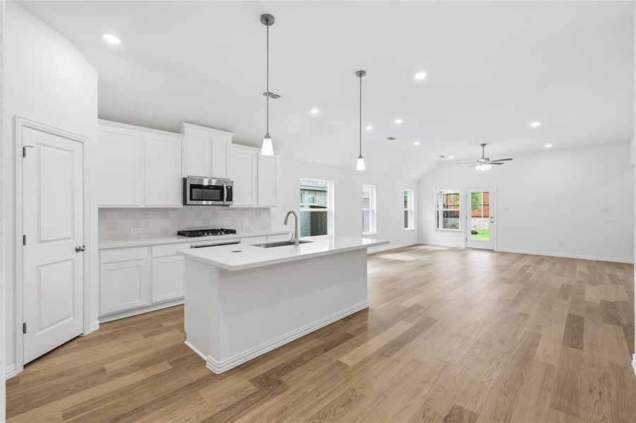 Bright open-concept kitchen and living area featuring wood-finish flooring, vaulted ceilings, and recessed lighting