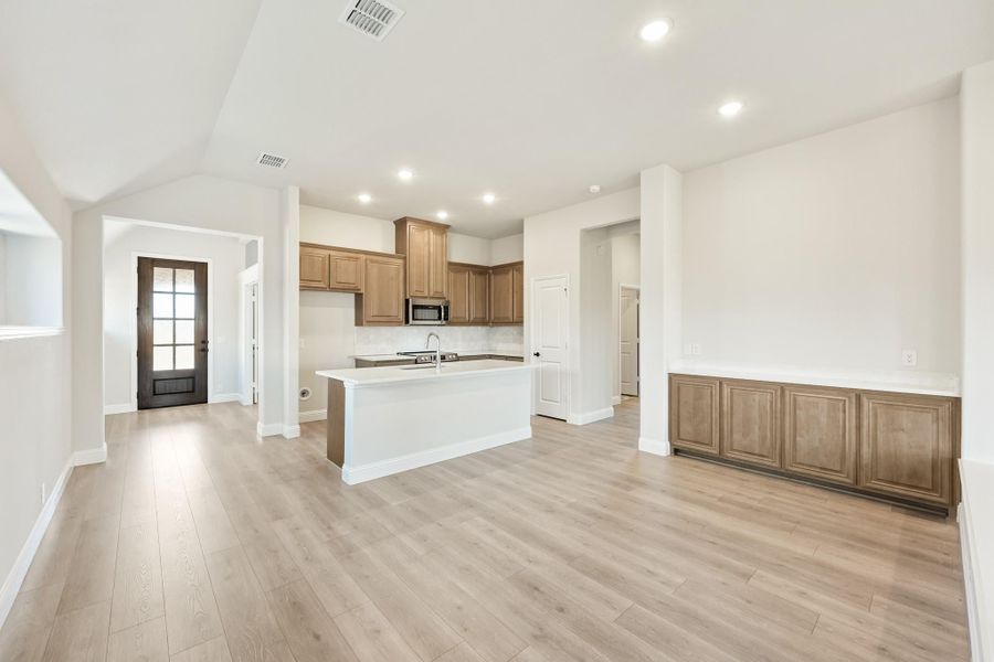 Open-concept kitchen with wood cabinets, white island, and light hardwood floors connecting to living area Open-concept kitchen with wood cabinets, white island, and light hardwood floors connecting to living area