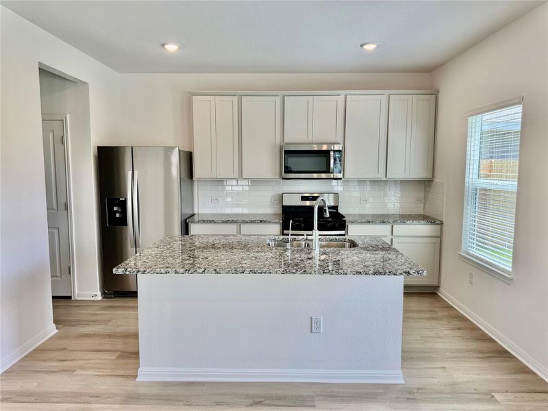 Kitchen with light stone counters, stainless steel appliances, light wood-style flooring, decorative backsplash, and recessed lighting Kitchen with light stone counters, stainless steel appliances, light wood-style flooring, decorative backsplash, and recessed lighting