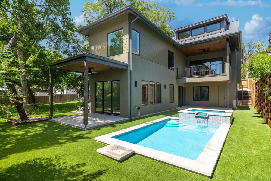 Contemporary exterior featuring a private pool with an integrated spa, expansive artificial turf, a covered patio with a ceiling fan, and a second-story balcony