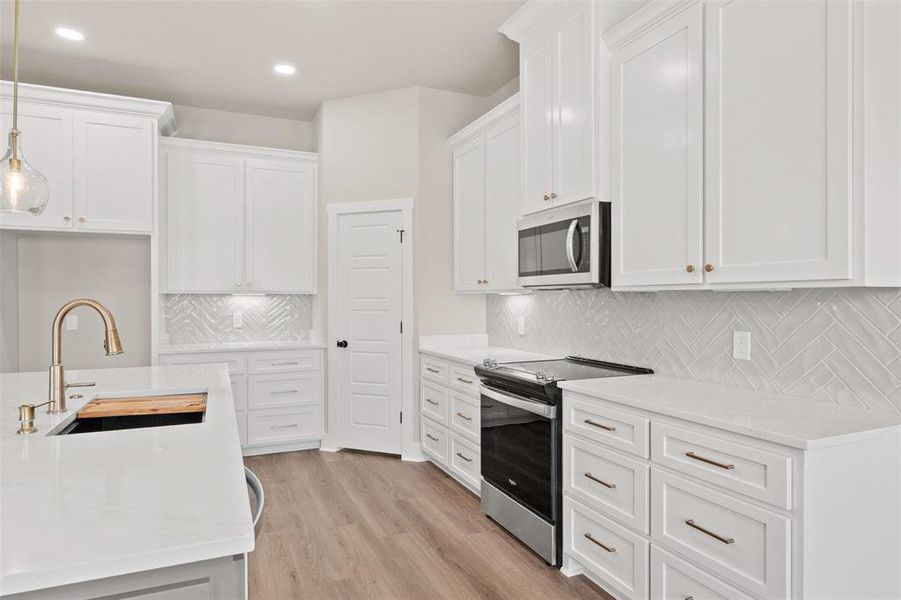 Kitchen featuring stainless steel appliances, white cabinetry, light stone countertops, and light wood-style flooring
