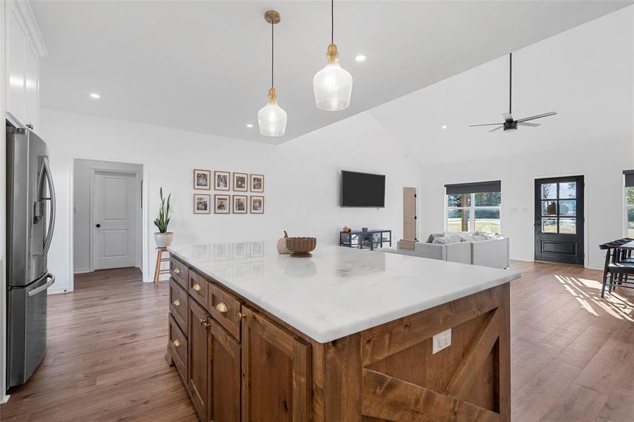 Kitchen with pendant lighting, lofted ceiling, light wood-type flooring, a kitchen island, and stainless steel refrigerator with ice dispenser