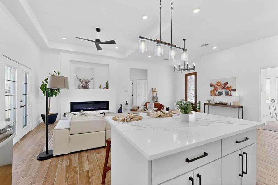Kitchen featuring a glass covered fireplace, light stone counters, open floor plan, light wood-style flooring, and recessed lighting
