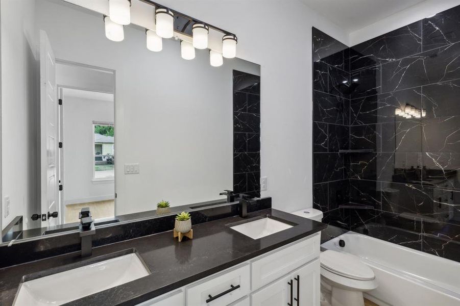 Full bathroom with dual vanity, tiled shower / bath, and toilet