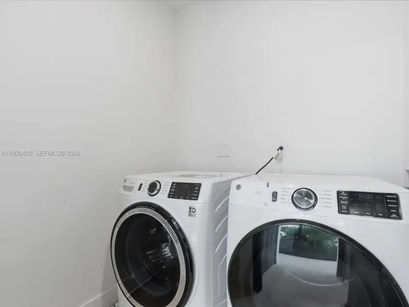 Dedicated laundry area featuring white front-loading high-efficiency appliances with glass-front doors and digital interface controls Dedicated laundry area featuring white front-loading high-efficiency appliances with glass-front doors and digital interface controls