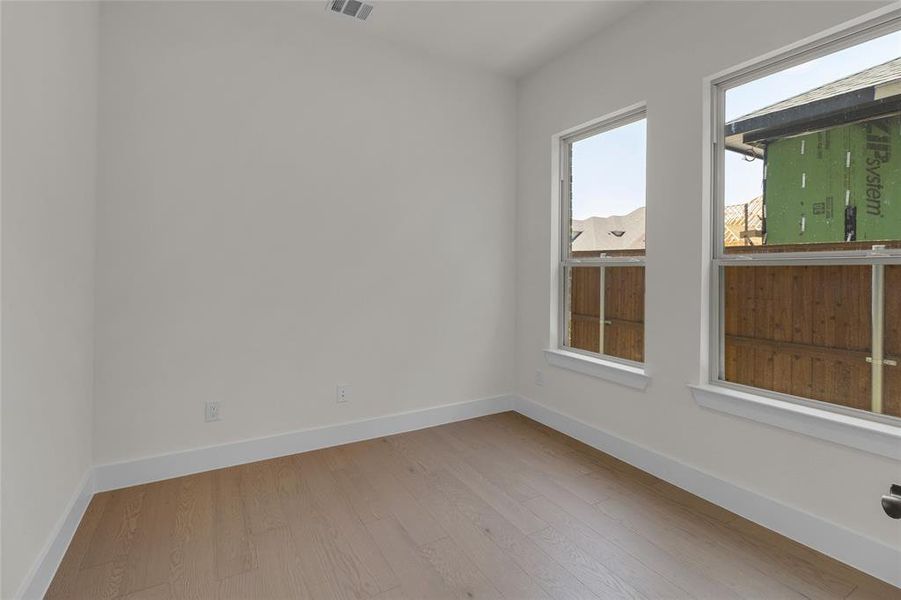 Bright room featuring two large windows, light wood-finish flooring, white walls, and white baseboards