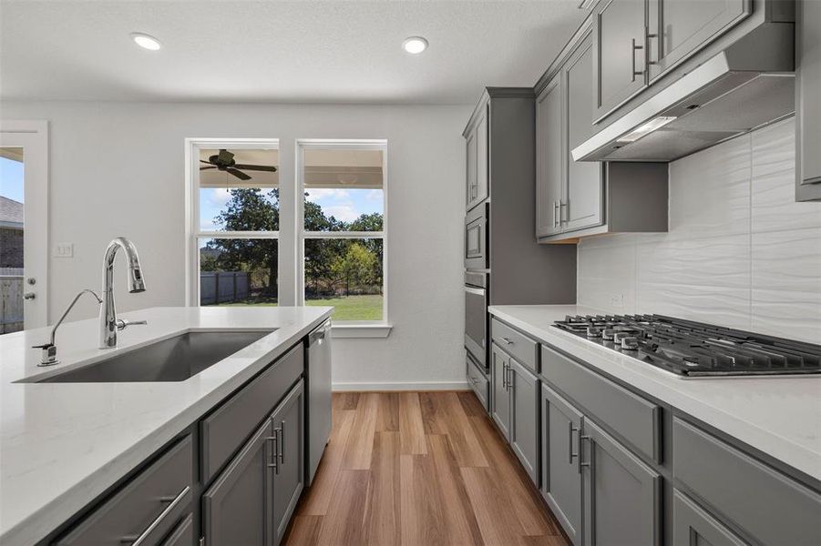 Kitchen with gray cabinets, under cabinet range hood, light stone countertops, decorative backsplash, and recessed lighting Kitchen with gray cabinets, under cabinet range hood, light stone countertops, decorative backsplash, and recessed lighting