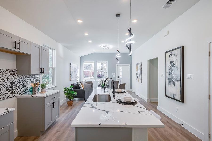 Kitchen with vaulted ceiling, sink, gray cabinets, hanging light fixtures, and an island with sink