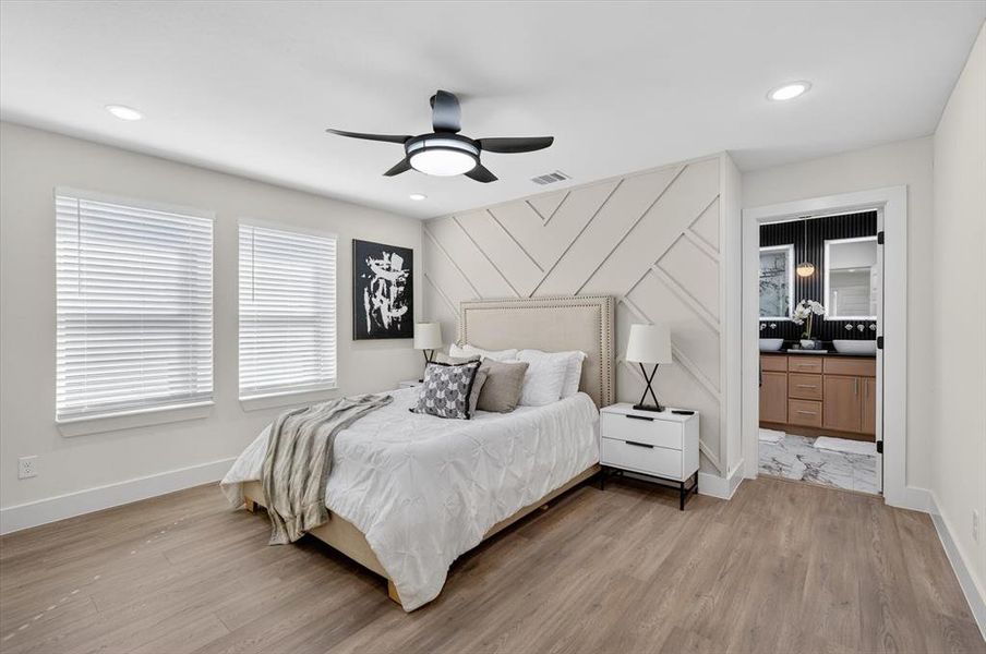 Bedroom featuring wood-finish flooring, two windows with blinds, and a textured accent wall