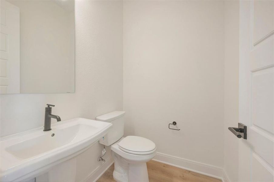 Contemporary powder room featuring a pedestal sink with a matte black faucet, a sleek toilet, and a large wall-mounted mirror