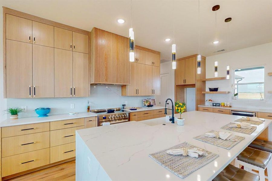 Kitchen featuring high end stainless steel range oven, light hardwood / wood flooring, light stone counters, and an island with sink