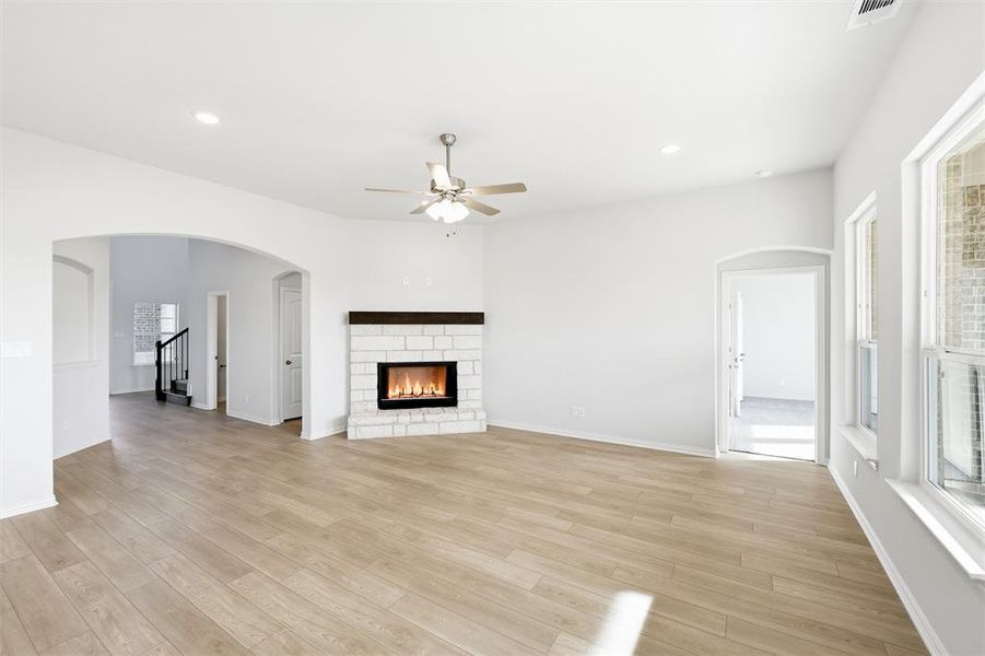 Unfurnished living room featuring arched walkways, a stone fireplace, light wood-style flooring, ceiling fan, and recessed lighting