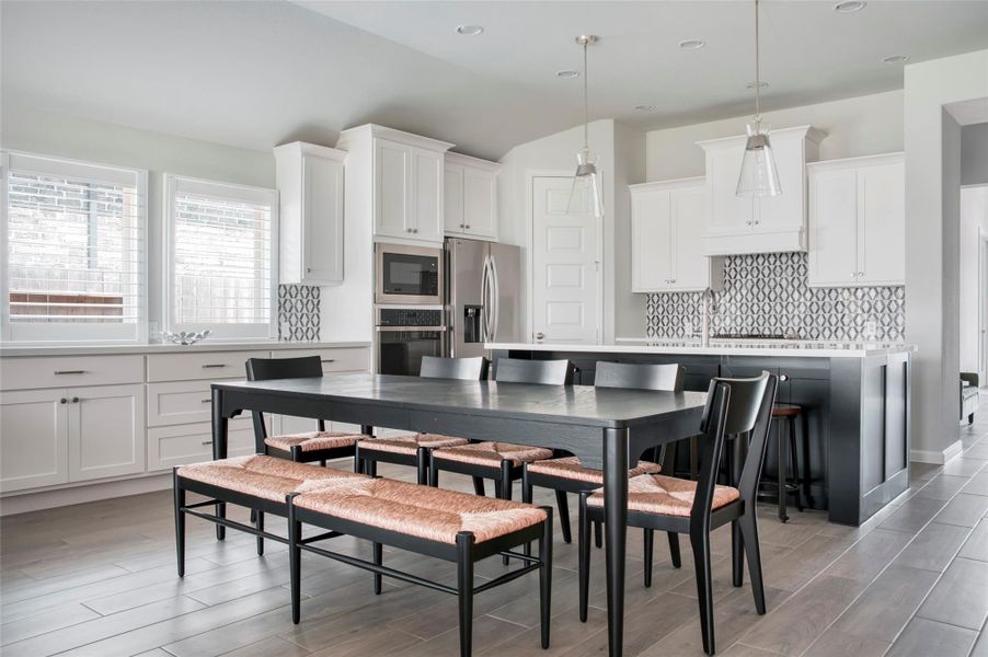 This modern kitchen features sleek white cabinetry, a stylish patterned backsplash, and stainless steel appliances. It includes a spacious island with pendant lighting, and a dining area with a large table and seating for six. The room is bright and airy with ample natural light from the windows. This modern kitchen features sleek white cabinetry, a stylish patterned backsplash, and stainless steel appliances. It includes a spacious island with pendant lighting, and a dining area with a large table and seating for six. The room is bright and airy with ample natural light from the windows.