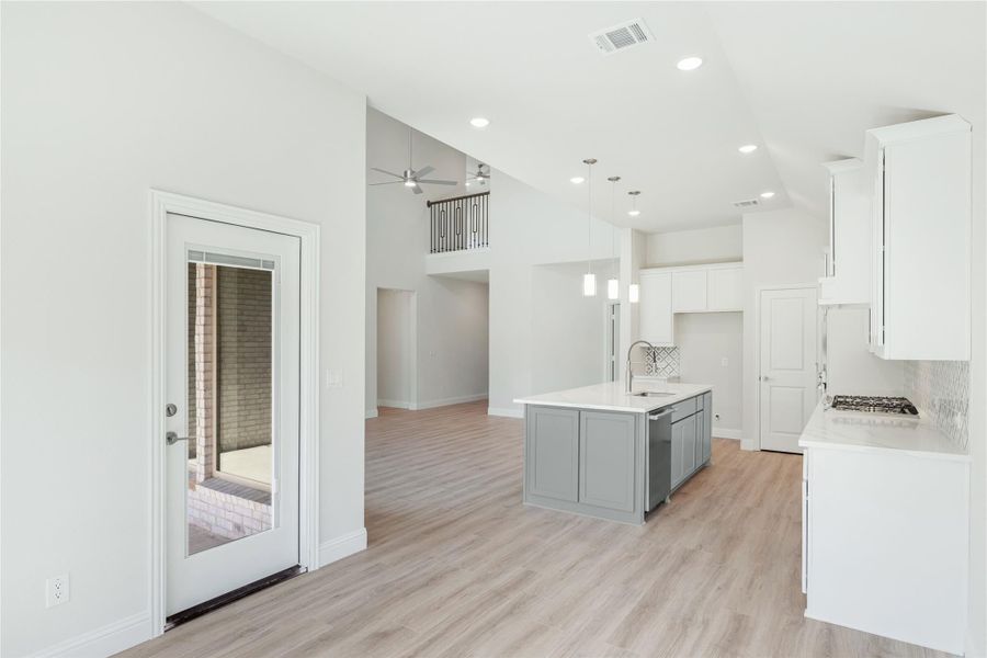 Open kitchen with gray island, white cabinets, light wood floors, and view into two-story living area