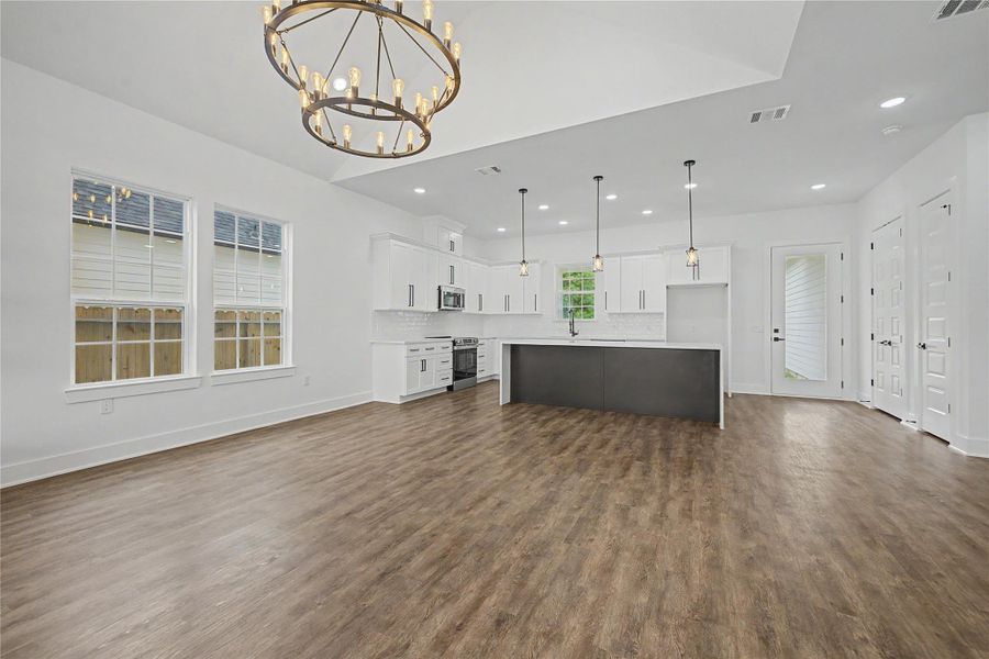 Open living and dining area with vaulted ceiling, statement chandelier, and warm wood-look flooring.