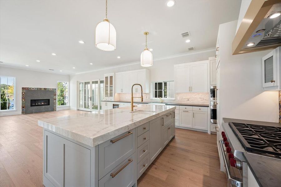 Kitchen featuring a large island, white cabinetry, range hood, light stone counters, and decorative light fixtures