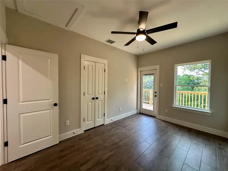 Unfurnished bedroom featuring access to exterior, dark wood-style floors, attic access, a ceiling fan, and a closet