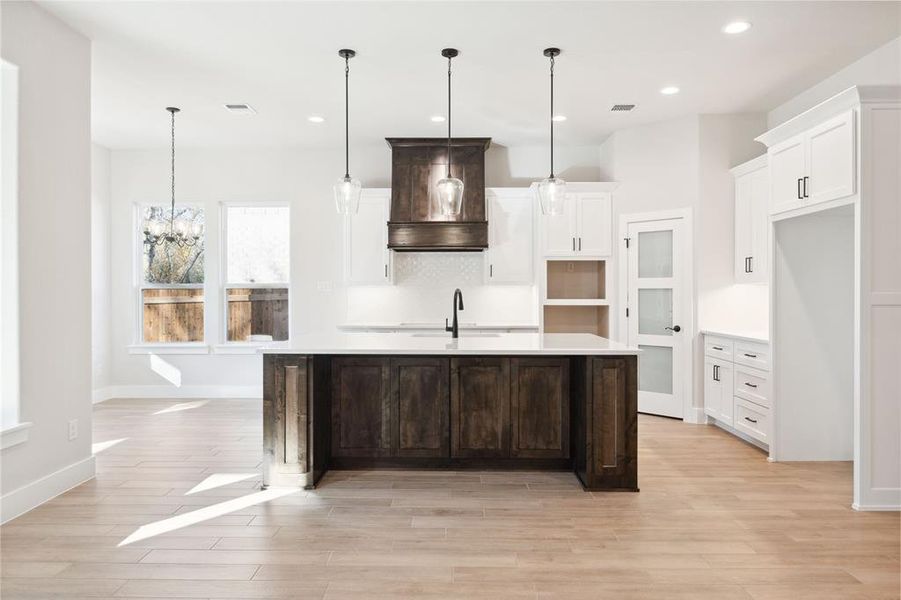 Kitchen with premium range hood, a kitchen island with sink, pendant lighting, and a notable chandelier