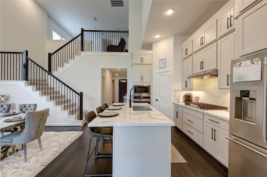 This modern home features an open-concept kitchen with sleek white cabinetry, a large island with seating, and stainless steel appliances. The adjacent dining area is elegantly designed, and a stylish staircase leads to the upper level, enhancing the space's contemporary feel.