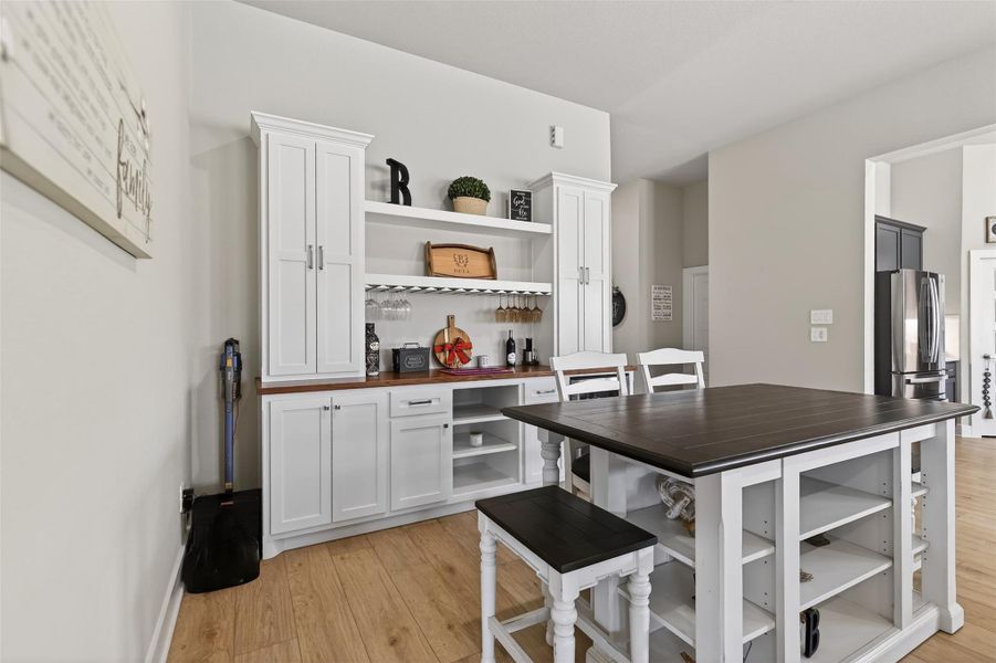 This photo showcases one example of the custom built-ins, additional eating area with  and barstool seating. This area can serve as a butler's pantry, as well as a trendy dining room with extra display shelving and drink fridge.
