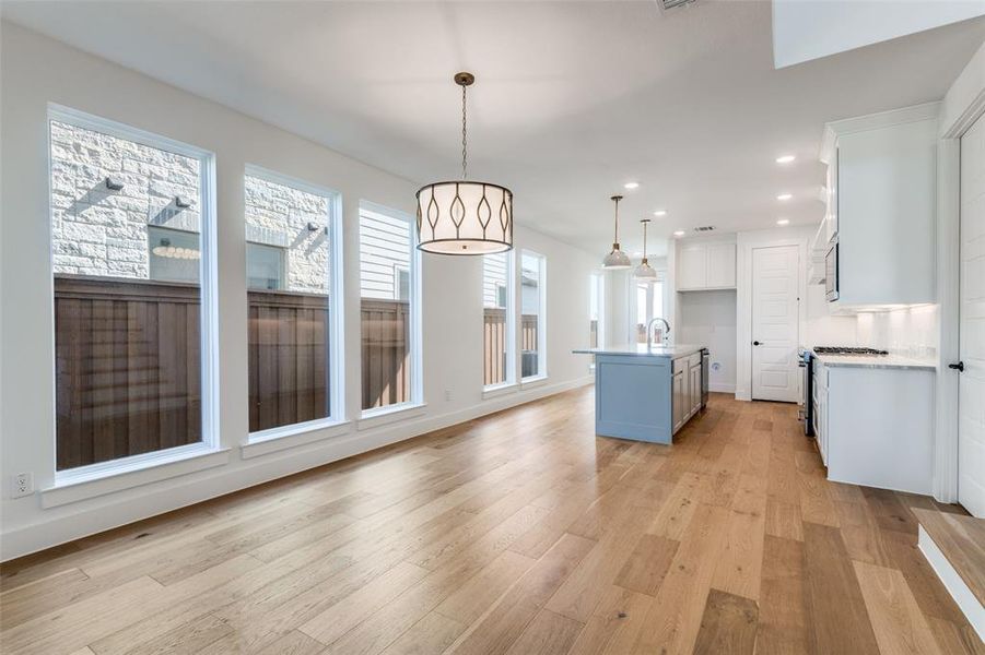 Kitchen featuring white cabinetry, hanging light fixtures, light hardwood / wood-style flooring, and a center island with sink