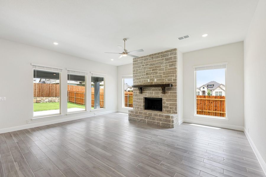 Open living room with floor-to-ceiling stone fireplace, wood-look floors, and large backyard-facing windows Open living room with floor-to-ceiling stone fireplace, wood-look floors, and large backyard-facing windows