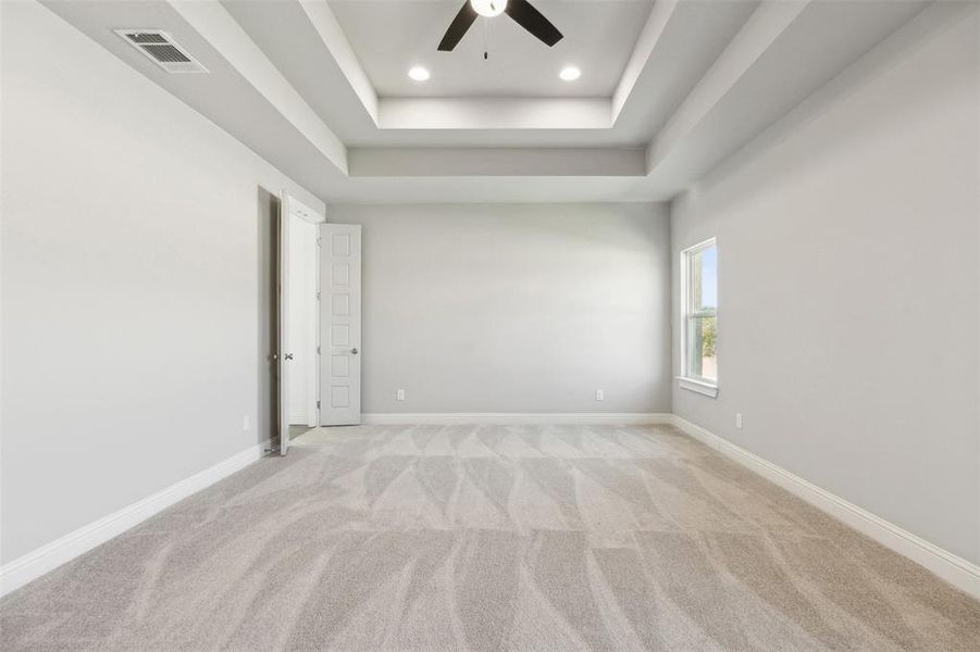 Carpeted spare room featuring ceiling fan and a raised ceiling