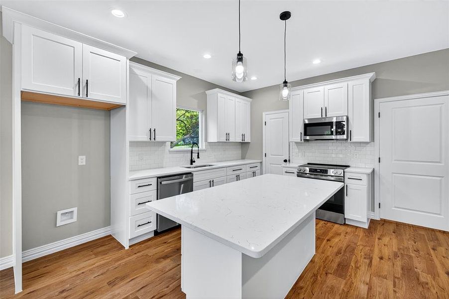 Kitchen with a kitchen island, stainless steel appliances, light stone counters, pendant lighting, and light wood finished floors Kitchen with a kitchen island, stainless steel appliances, light stone counters, pendant lighting, and light wood finished floors