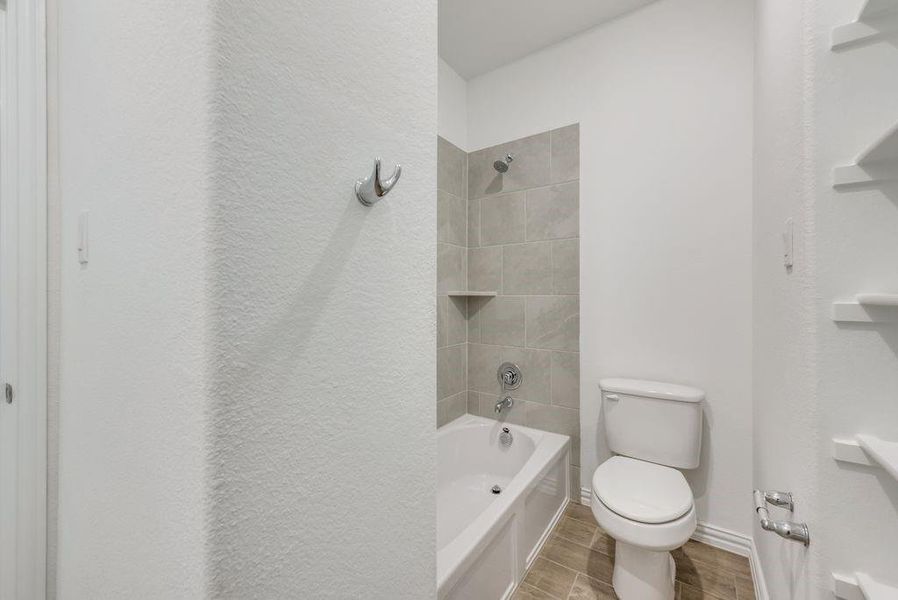 Bathroom with tiled shower / bath, toilet, and tile patterned floors