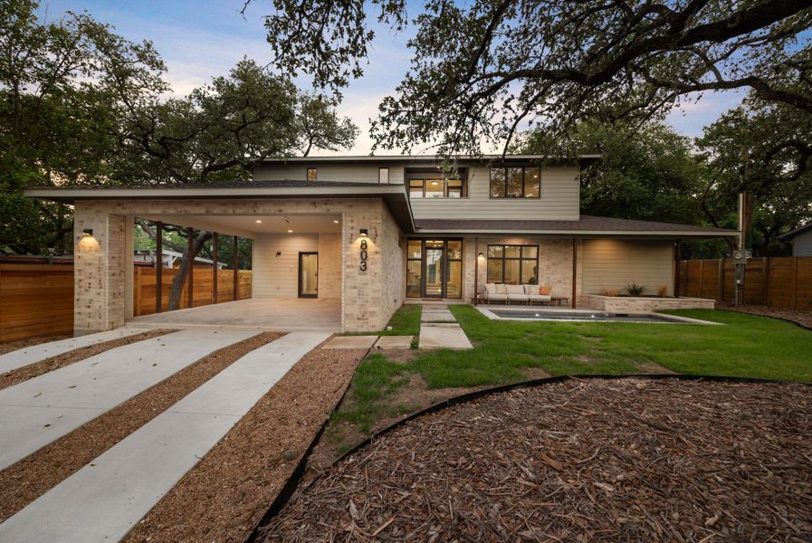 Rear view of property with a carport, driveway, brick siding, a patio, and roof with shingles